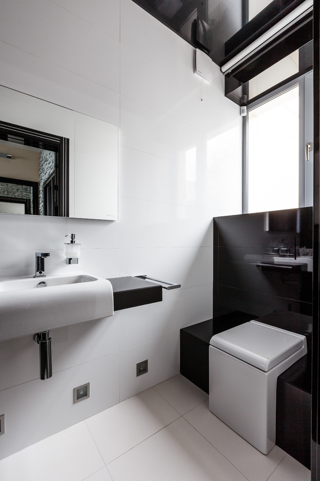 Photo of a contemporary powder room in Other with a two-piece toilet, white tile, black tile, an integrated sink and white floor.