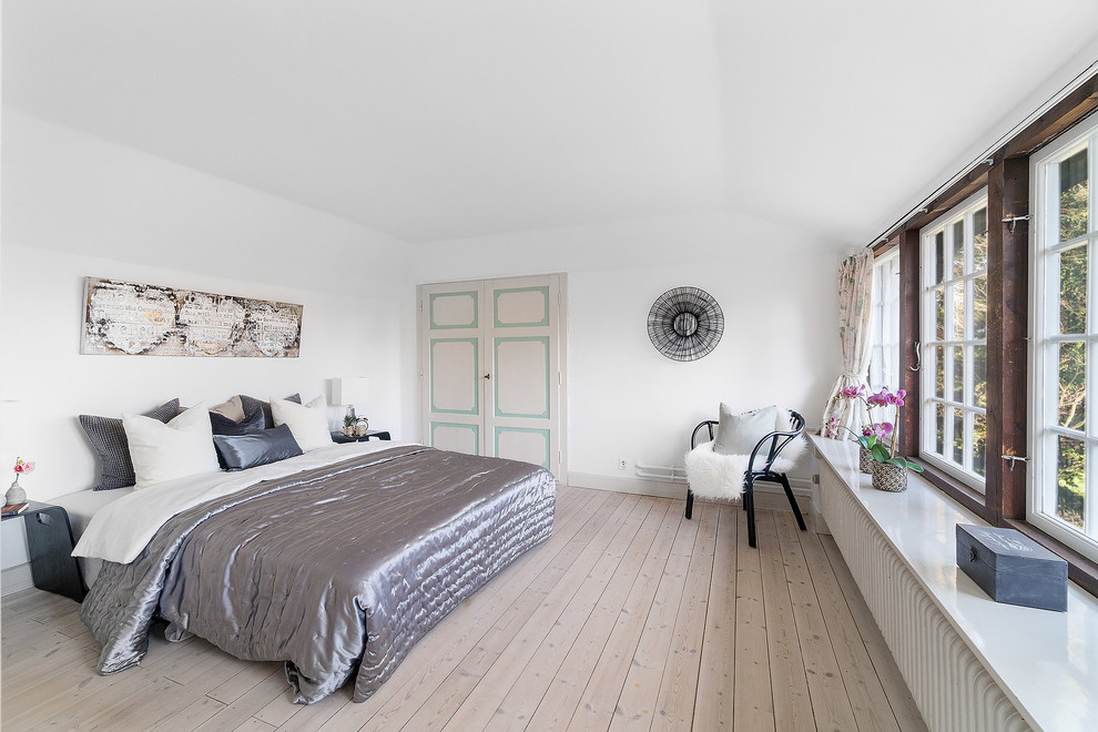 This is an example of a country master bedroom in Copenhagen with white walls, light hardwood floors and beige floor.