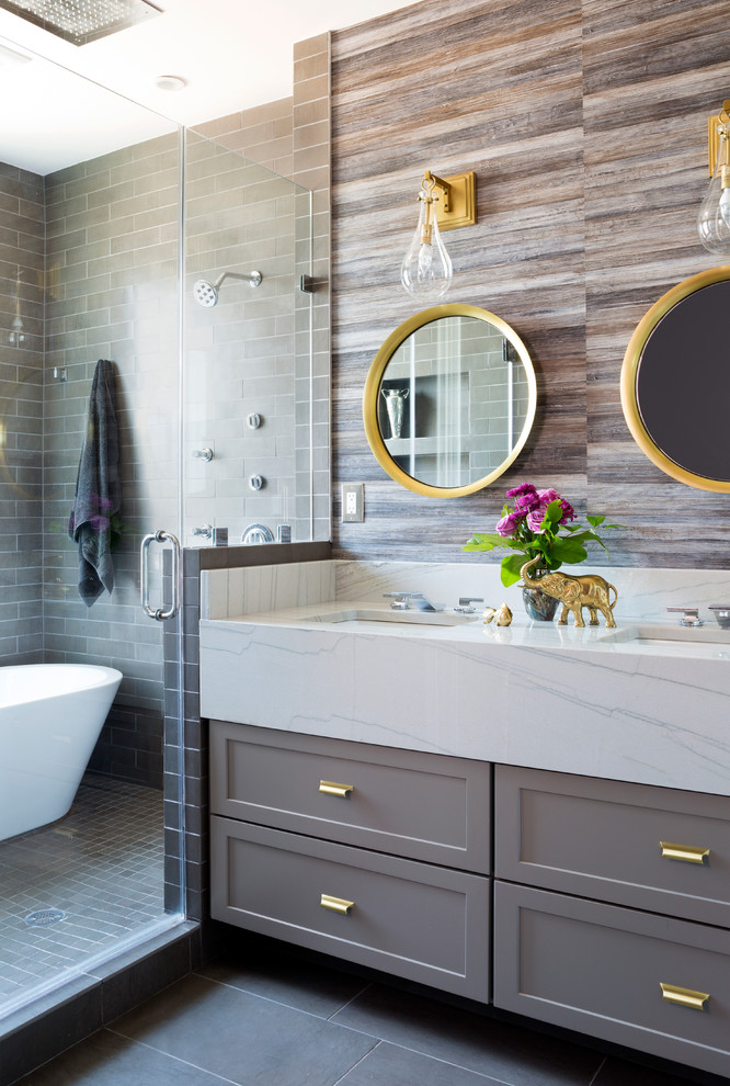Photo of a mid-sized transitional master bathroom in DC Metro with grey cabinets, subway tile, flat-panel cabinets, a freestanding tub, an alcove shower, a one-piece toilet, white tile, porcelain floors, an integrated sink, marble benchtops, brown walls and a hinged shower door.