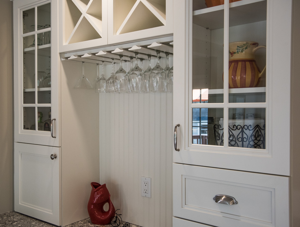 Example of a mid-sized transitional l-shaped medium tone wood floor eat-in kitchen design in Boston with a farmhouse sink, shaker cabinets, white cabinets, quartz countertops, white backsplash, subway tile backsplash, stainless steel appliances and an island
