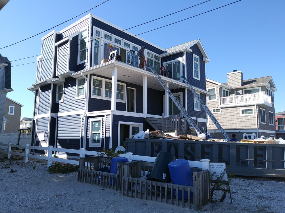 Aménagement d'une grande façade de maison bleue bord de mer en bardage à clin à deux étages et plus avec un revêtement en vinyle, un toit plat, un toit en shingle et un toit noir.