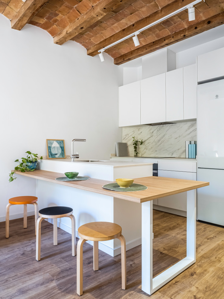 Photo of a mid-sized mediterranean galley eat-in kitchen in Barcelona with an undermount sink, flat-panel cabinets, white cabinets, marble benchtops, grey splashback, marble splashback, white appliances, light hardwood floors, a peninsula, white benchtop and wood.
