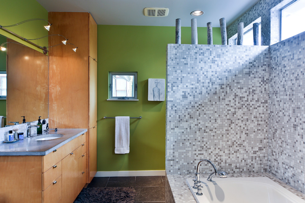 Photo of a mid-sized contemporary master bathroom in Houston with flat-panel cabinets, light wood cabinets, a drop-in tub, an open shower, a one-piece toilet, gray tile, glass tile, green walls, slate floors, a drop-in sink and concrete benchtops.