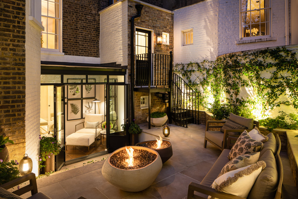 This is an example of a small traditional back patio in London with a fireplace and natural stone paving.