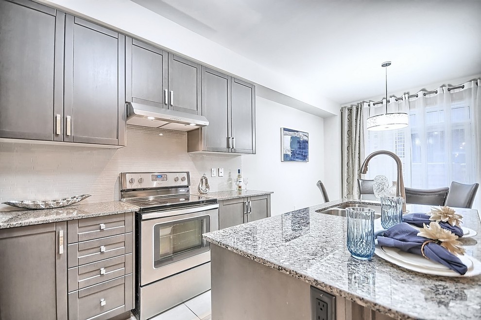 Open concept kitchen - mid-sized transitional l-shaped ceramic tile and beige floor open concept kitchen idea in Toronto with an undermount sink, shaker cabinets, gray cabinets, granite countertops, beige backsplash, mosaic tile backsplash, stainless steel appliances and an island