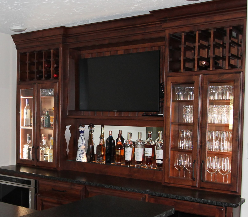 Example of a large mountain style wet bar design with an undermount sink, raised-panel cabinets, medium tone wood cabinets, granite countertops and black countertops