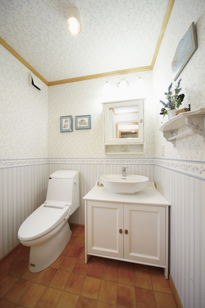 This is an example of a traditional powder room in Tokyo Suburbs with recessed-panel cabinets, white cabinets, multi-coloured walls, terra-cotta floors, a vessel sink and orange floor.