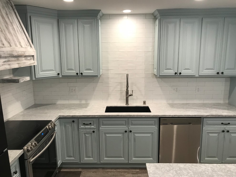 This is an example of a mid-sized country l-shaped eat-in kitchen in Sacramento with an undermount sink, raised-panel cabinets, blue cabinets, marble benchtops, white splashback, porcelain splashback, stainless steel appliances, laminate floors, with island, grey floor and grey benchtop.