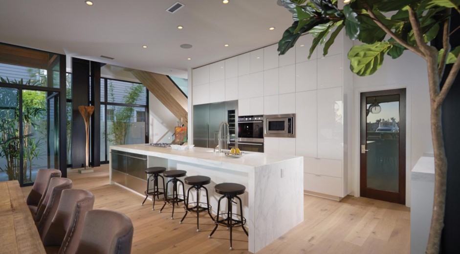 This is an example of a large modern galley open plan kitchen in Orange County with an undermount sink, flat-panel cabinets, white cabinets, marble benchtops, stainless steel appliances, light hardwood floors, with island and brown floor.