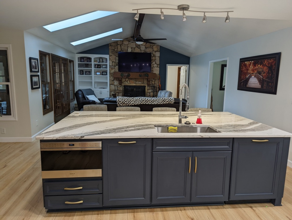 Bild på ett stort funkis vit linjärt vitt kök och matrum, med en enkel diskho, skåp i shakerstil, blå skåp, bänkskiva i kvartsit, grått stänkskydd, stänkskydd i glaskakel, rostfria vitvaror, vinylgolv, en köksö och beiget golv