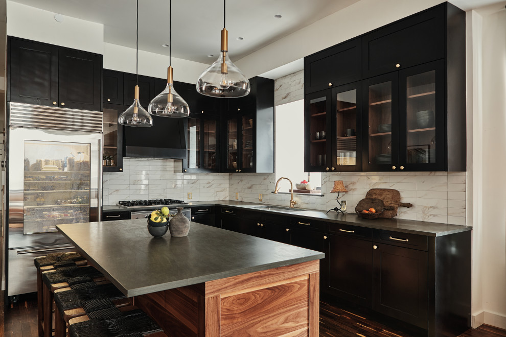 Inredning av ett modernt grå grått l-kök, med en undermonterad diskho, skåp i shakerstil, svarta skåp, vitt stänkskydd, rostfria vitvaror, mörkt trägolv, en köksö och brunt golv