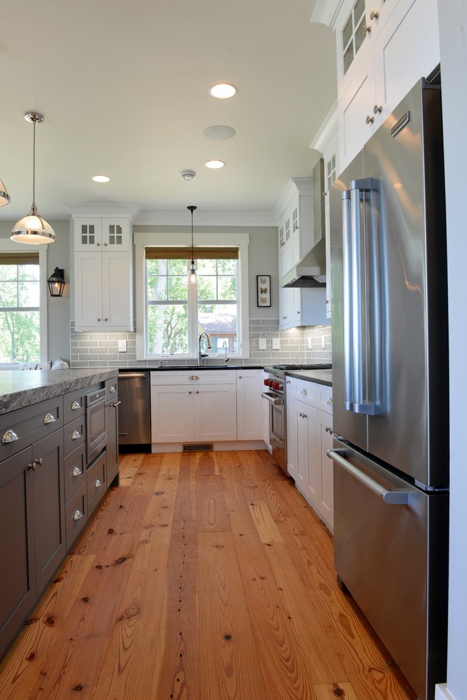 Example of a mid-sized transitional l-shaped light wood floor eat-in kitchen design with shaker cabinets, white cabinets, granite countertops, gray backsplash, subway tile backsplash, stainless steel appliances, an island and an undermount sink