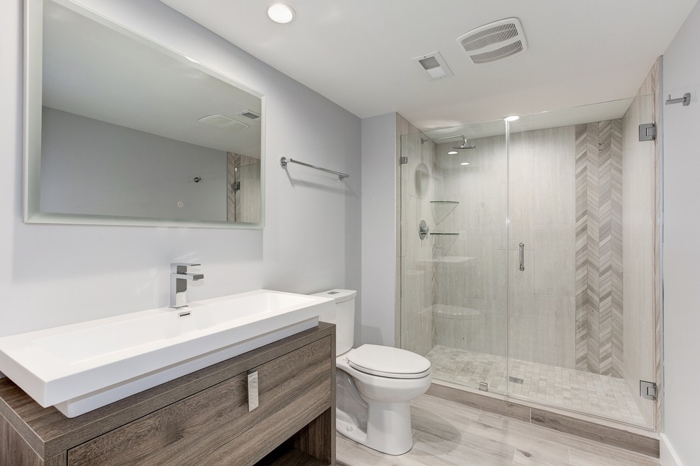 Photo of a medium sized traditional grey and white ensuite bathroom in DC Metro with flat-panel cabinets, an alcove shower, a two-piece toilet, grey walls, porcelain flooring, engineered stone worktops, grey floors, a hinged door, white worktops, a single sink, a freestanding vanity unit, medium wood cabinets, beige tiles, porcelain tiles, a vessel sink and feature lighting.