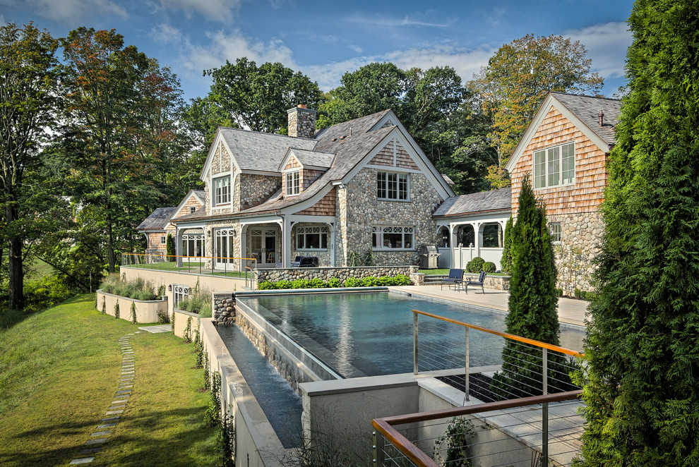 This is an example of an expansive transitional backyard rectangular infinity pool in New York with a pool house and concrete pavers.