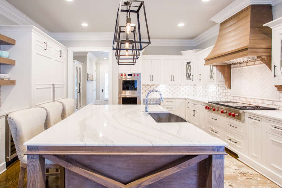 Example of a large transitional u-shaped medium tone wood floor and brown floor eat-in kitchen design in Atlanta with a farmhouse sink, raised-panel cabinets, white cabinets, quartz countertops, white backsplash, brick backsplash, stainless steel appliances, an island and white countertops