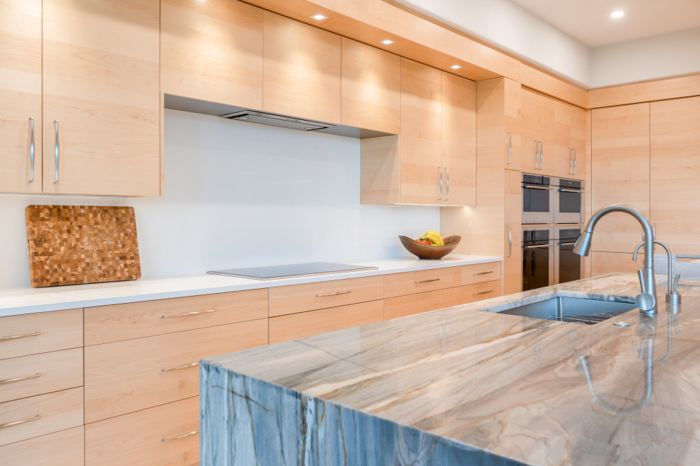Large contemporary u-shaped kitchen/diner in Other with a submerged sink, flat-panel cabinets, light wood cabinets, white splashback, integrated appliances, light hardwood flooring, an island, beige floors and grey worktops.