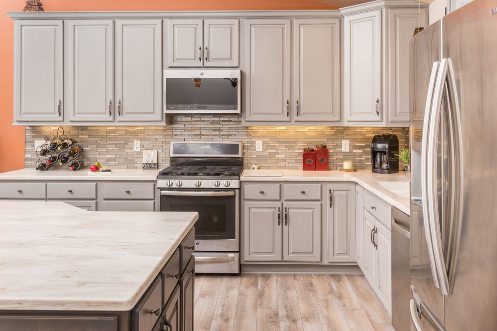 Example of a mid-sized transitional l-shaped open concept kitchen design with an undermount sink, raised-panel cabinets, gray cabinets, solid surface countertops, metallic backsplash, mosaic tile backsplash, stainless steel appliances and an island