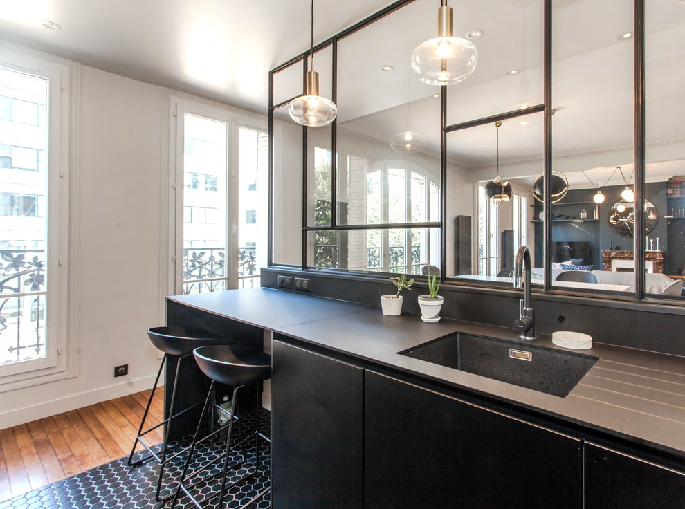 This is an example of a mid-sized contemporary single-wall open plan kitchen in Paris with an undermount sink, black cabinets, porcelain floors, with island, black floor and black benchtop.