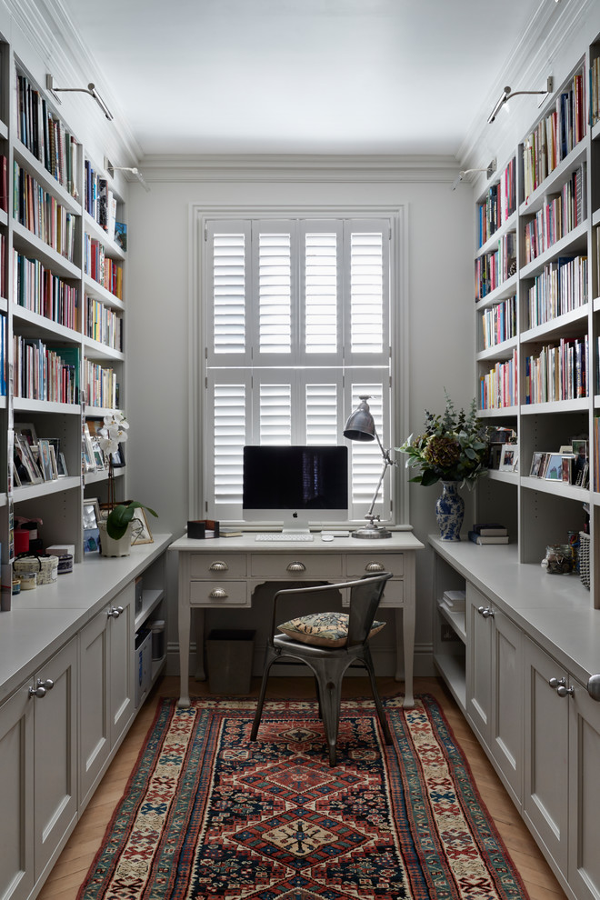 Design ideas for a mid-sized transitional home office in London with grey walls, light hardwood floors, a freestanding desk, beige floor and a library.
