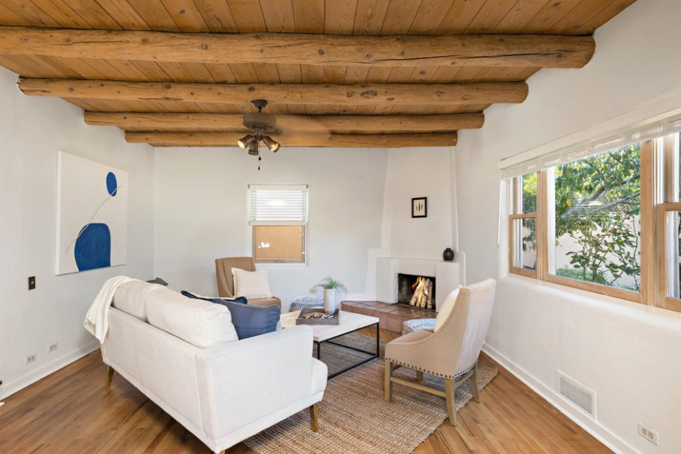 Foto på ett mellanstort amerikanskt separat vardagsrum, med vita väggar, mellanmörkt trägolv, en öppen hörnspis, en spiselkrans i gips och brunt golv