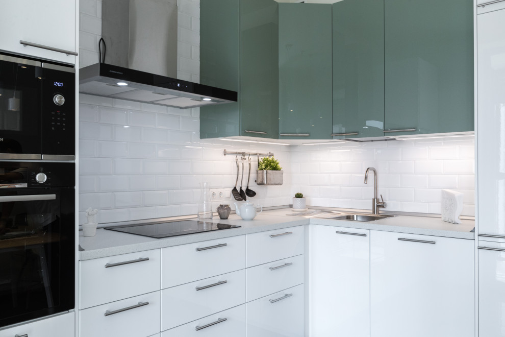 This is an example of a scandinavian l-shaped kitchen in Moscow with flat-panel cabinets, green cabinets, white splashback, subway tile splashback, black appliances and white benchtop.