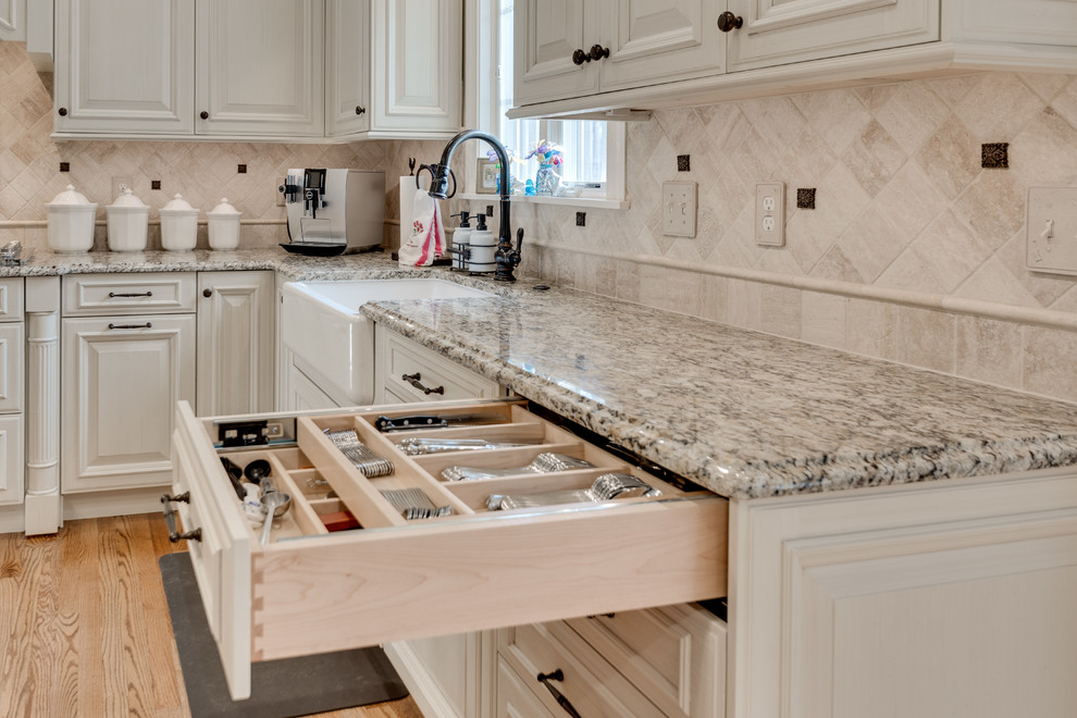 Design ideas for a large traditional kitchen in Baltimore with a farmhouse sink, raised-panel cabinets, granite benchtops, beige splashback, travertine splashback, stainless steel appliances, light hardwood floors and with island.