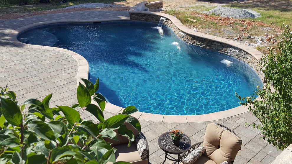 Design ideas for a mid-sized traditional backyard custom-shaped natural pool in Other with a water feature and concrete pavers.