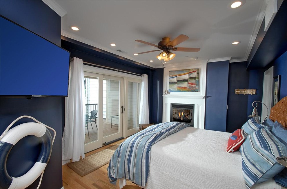 This is an example of a mid-sized beach style master bedroom in New York with blue walls, light hardwood floors, a standard fireplace and a plaster fireplace surround.