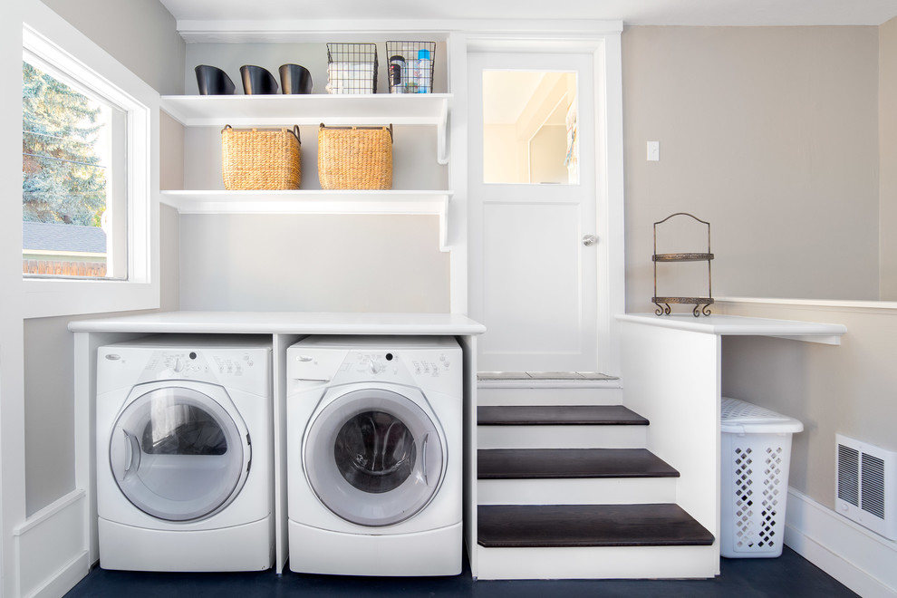 Large transitional dedicated laundry room in Boise with white cabinets, laminate benchtops, concrete floors, a side-by-side washer and dryer, open cabinets, black floor, white benchtop and grey walls.