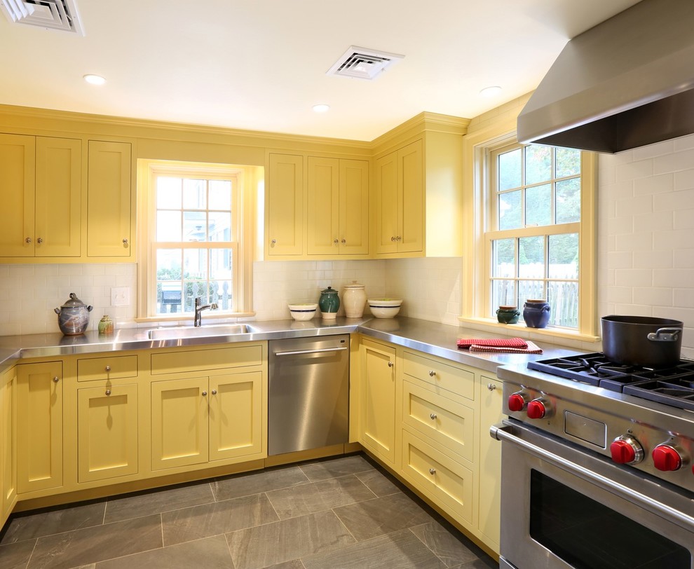This is an example of a mid-sized traditional u-shaped separate kitchen in New York with an integrated sink, recessed-panel cabinets, yellow cabinets, stainless steel benchtops, white splashback, subway tile splashback, stainless steel appliances, porcelain floors and grey floor.