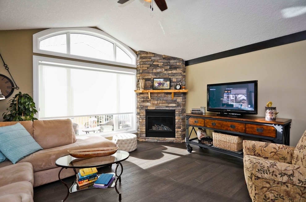 Inspiration for a mid-sized transitional enclosed family room in Calgary with beige walls, dark hardwood floors, a corner fireplace, a stone fireplace surround and a freestanding tv.