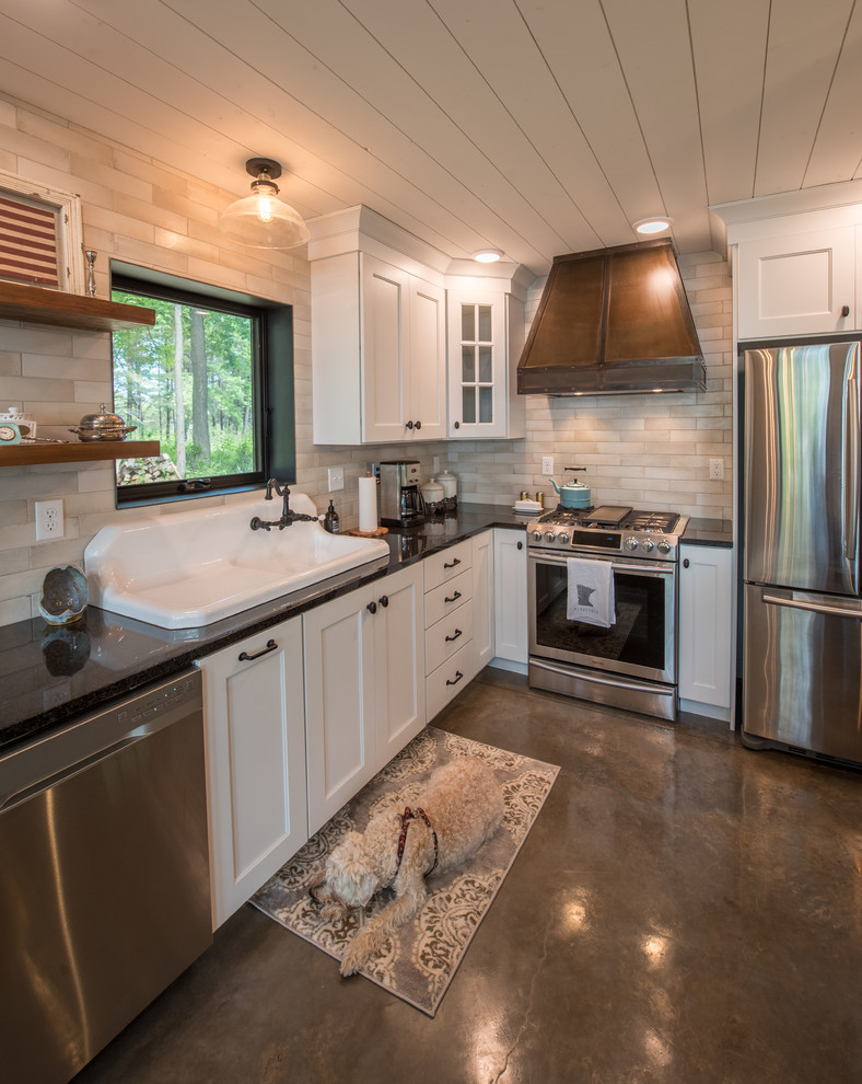 Inspiration for a mid-sized country l-shaped open plan kitchen in Minneapolis with a drop-in sink, shaker cabinets, white cabinets, solid surface benchtops, beige splashback, subway tile splashback, stainless steel appliances, concrete floors, with island, grey floor and black benchtop.