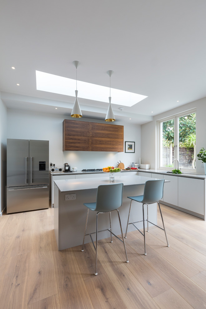 Mid-sized contemporary l-shaped open plan kitchen in London with flat-panel cabinets, white cabinets, quartzite benchtops, white splashback, glass sheet splashback, light hardwood floors, with island, beige floor and white benchtop.