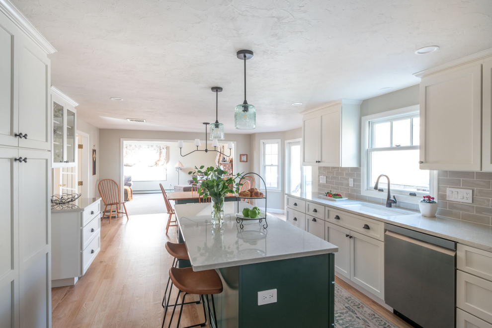 Eat-in kitchen - large transitional galley light wood floor and brown floor eat-in kitchen idea in Boston with an undermount sink, shaker cabinets, white cabinets, quartz countertops, beige backsplash, ceramic backsplash, stainless steel appliances, an island and white countertops