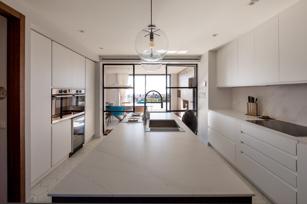 This is an example of a large modern single-wall eat-in kitchen in Barcelona with an undermount sink, flat-panel cabinets, white cabinets, quartz benchtops, white splashback, marble splashback, stainless steel appliances, porcelain floors, with island and grey floor.