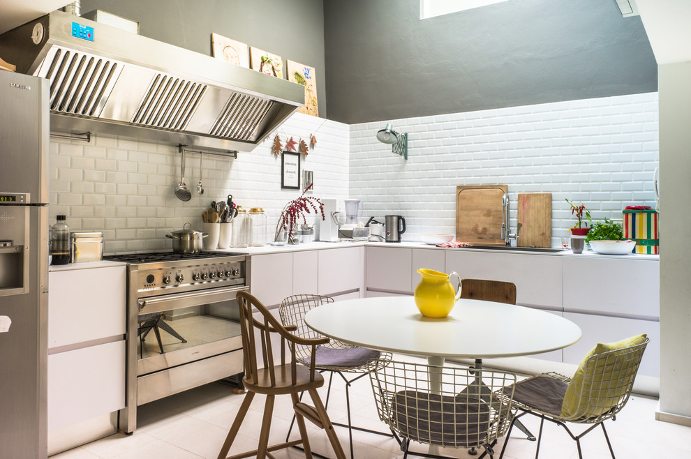 This is an example of a small contemporary l-shaped eat-in kitchen in Venice with a drop-in sink, flat-panel cabinets, white cabinets, white splashback, subway tile splashback, stainless steel appliances, no island, ceramic floors and white floor.