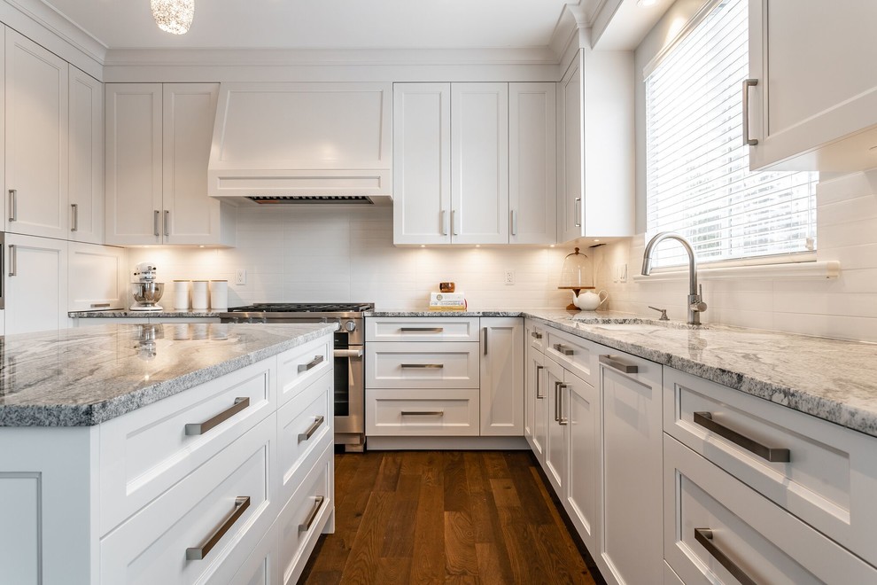 Large transitional u-shaped medium tone wood floor and brown floor eat-in kitchen photo in Vancouver with an undermount sink, recessed-panel cabinets, white cabinets, granite countertops, white backsplash, subway tile backsplash, stainless steel appliances, an island and multicolored countertops