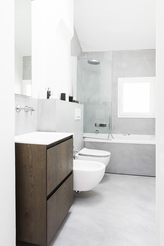 This is an example of a mid-sized contemporary master bathroom in Bologna with flat-panel cabinets, dark wood cabinets, a drop-in tub, a wall-mount toilet, grey walls, concrete floors, an integrated sink, solid surface benchtops, grey floor and a hinged shower door.
