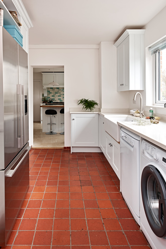 This is an example of a mid-sized transitional dedicated laundry room in Wiltshire with recessed-panel cabinets, white cabinets, terra-cotta floors, a side-by-side washer and dryer and red floor.