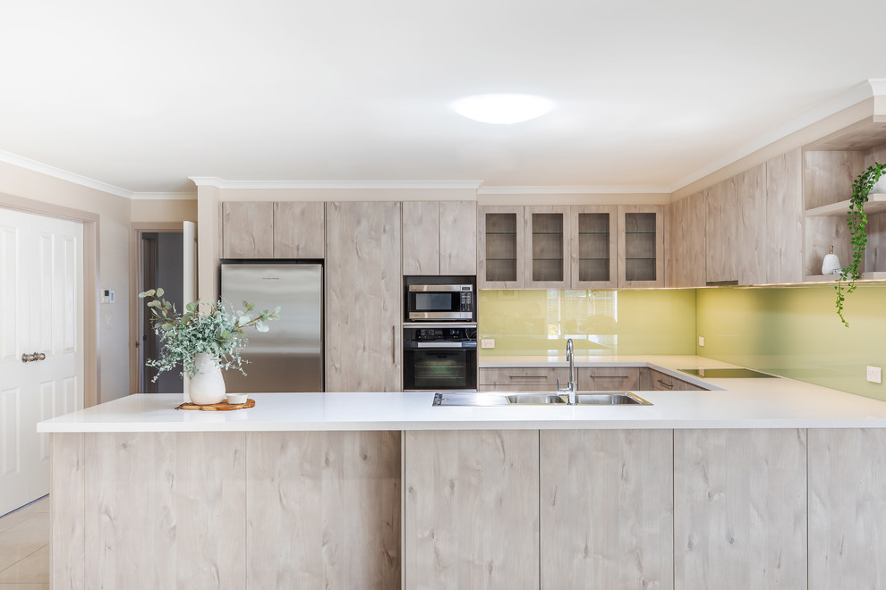 Inspiration for a mid-sized modern u-shaped kitchen pantry in Adelaide with a double-bowl sink, flat-panel cabinets, light wood cabinets, quartz benchtops, green splashback, glass sheet splashback, stainless steel appliances, porcelain floors, a peninsula, white floor and white benchtop.