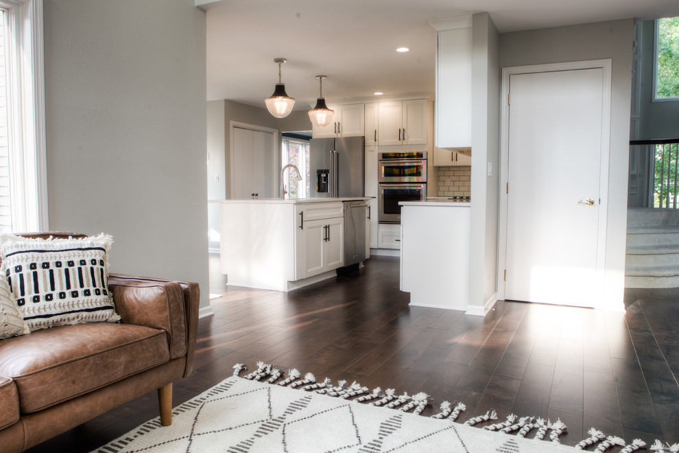 Large transitional l-shaped dark wood floor and brown floor home design photo with an undermount sink, recessed-panel cabinets, white cabinets, quartz countertops, white backsplash, subway tile backsplash, stainless steel appliances and an island
