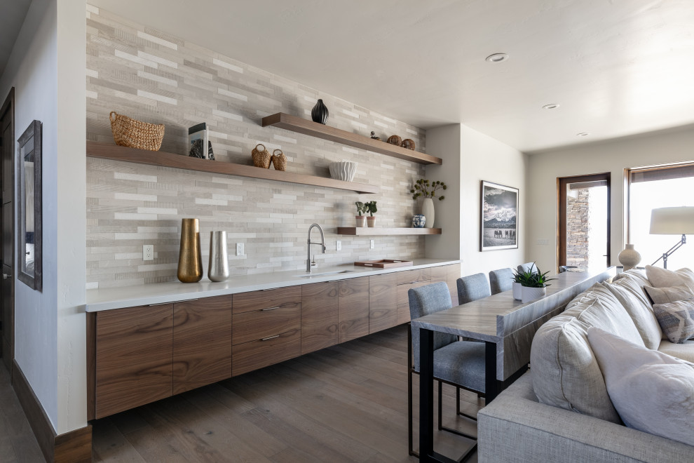 This is an example of a contemporary single-wall wet bar in Salt Lake City with an undermount sink, flat-panel cabinets, dark wood cabinets, grey splashback, medium hardwood floors, brown floor and white benchtop.