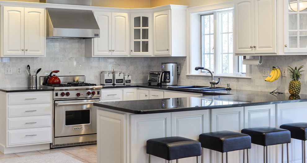 Kitchen - mid-sized transitional l-shaped kitchen idea in Boston with raised-panel cabinets, white cabinets, granite countertops, marble backsplash, stainless steel appliances and black countertops