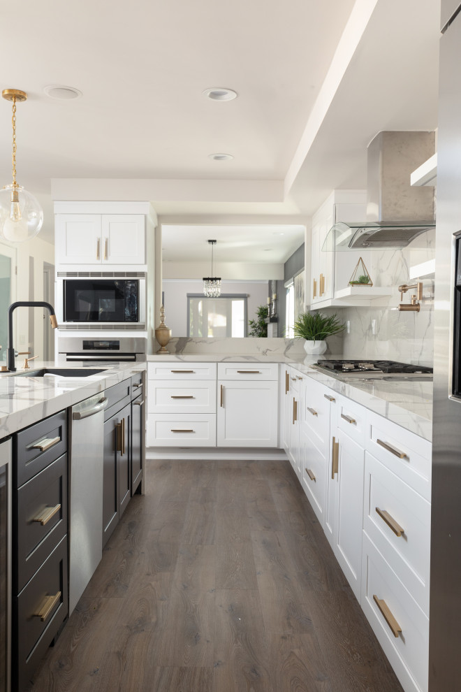 Inspiration for a mid-sized contemporary l-shaped open plan kitchen in Orange County with shaker cabinets, white cabinets, white splashback, porcelain splashback, stainless steel appliances, light hardwood floors, with island, brown floor and white benchtop.