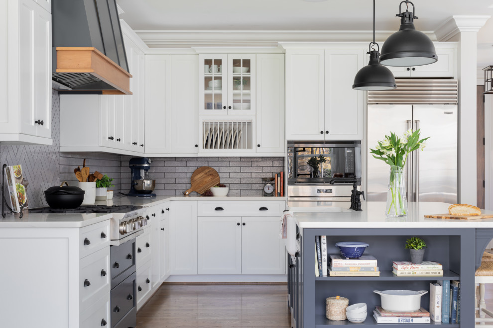 This is an example of a traditional kitchen in Other with a belfast sink, shaker cabinets, white cabinets, engineered stone countertops, grey splashback, metro tiled splashback, stainless steel appliances, medium hardwood flooring, brown floors and white worktops.