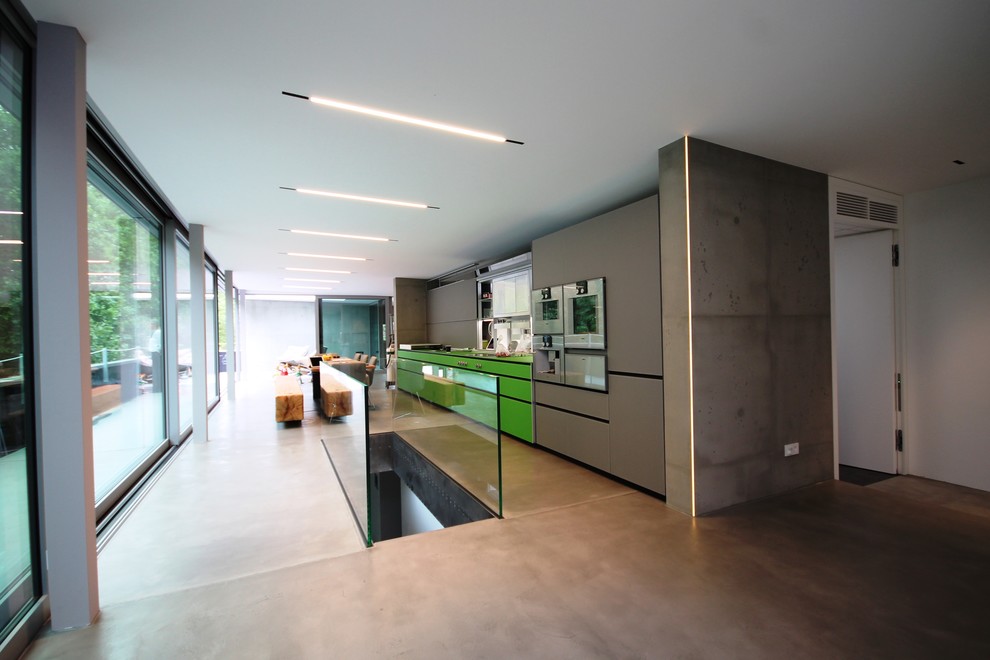 Offene, Einzeilige, Geräumige Industrial Küche ohne Insel mit integriertem Waschbecken, grünen Schränken, Mineralwerkstoff-Arbeitsplatte, Küchenrückwand in Grau, Küchengeräten aus Edelstahl und Betonboden in Stuttgart