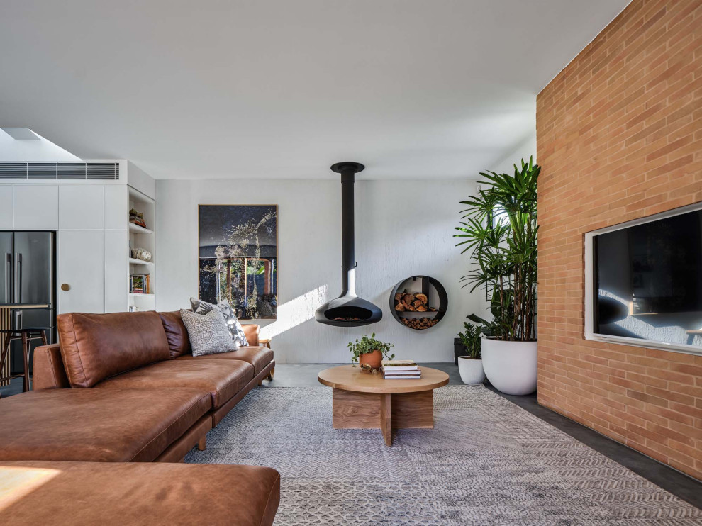 Источник вдохновения для домашнего уюта: гостиная комната в современном стиле с серыми стенами, подвесным камином, телевизором на стене, серым полом, кирпичными стенами и коричневым диваном