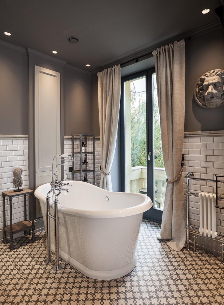 Photo of a mid-sized transitional master bathroom in London with a freestanding tub, subway tile, grey walls, shaker cabinets, grey cabinets, an open shower, gray tile, porcelain floors and a wall-mount sink.