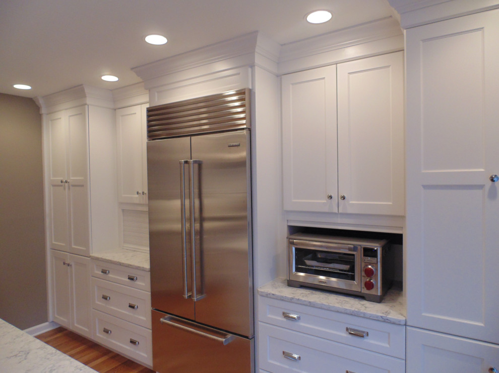Large transitional u-shaped medium tone wood floor and brown floor eat-in kitchen photo with an undermount sink, recessed-panel cabinets, white cabinets, quartz countertops, white backsplash, subway tile backsplash, stainless steel appliances, an island and white countertops