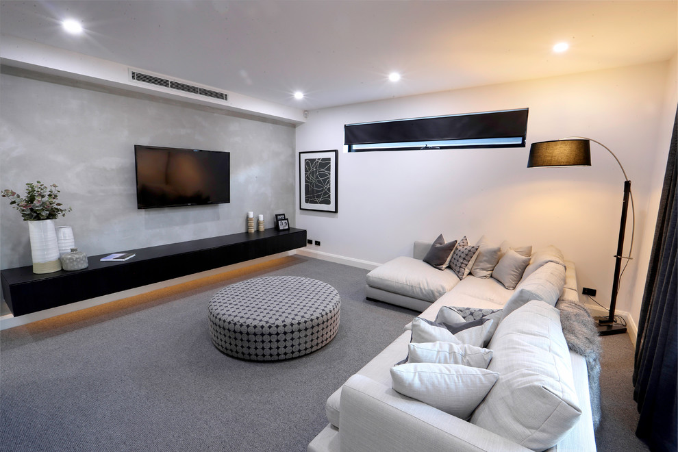 This is an example of a large industrial enclosed home theatre in Melbourne with grey walls, carpet, a wall-mounted tv and grey floor.